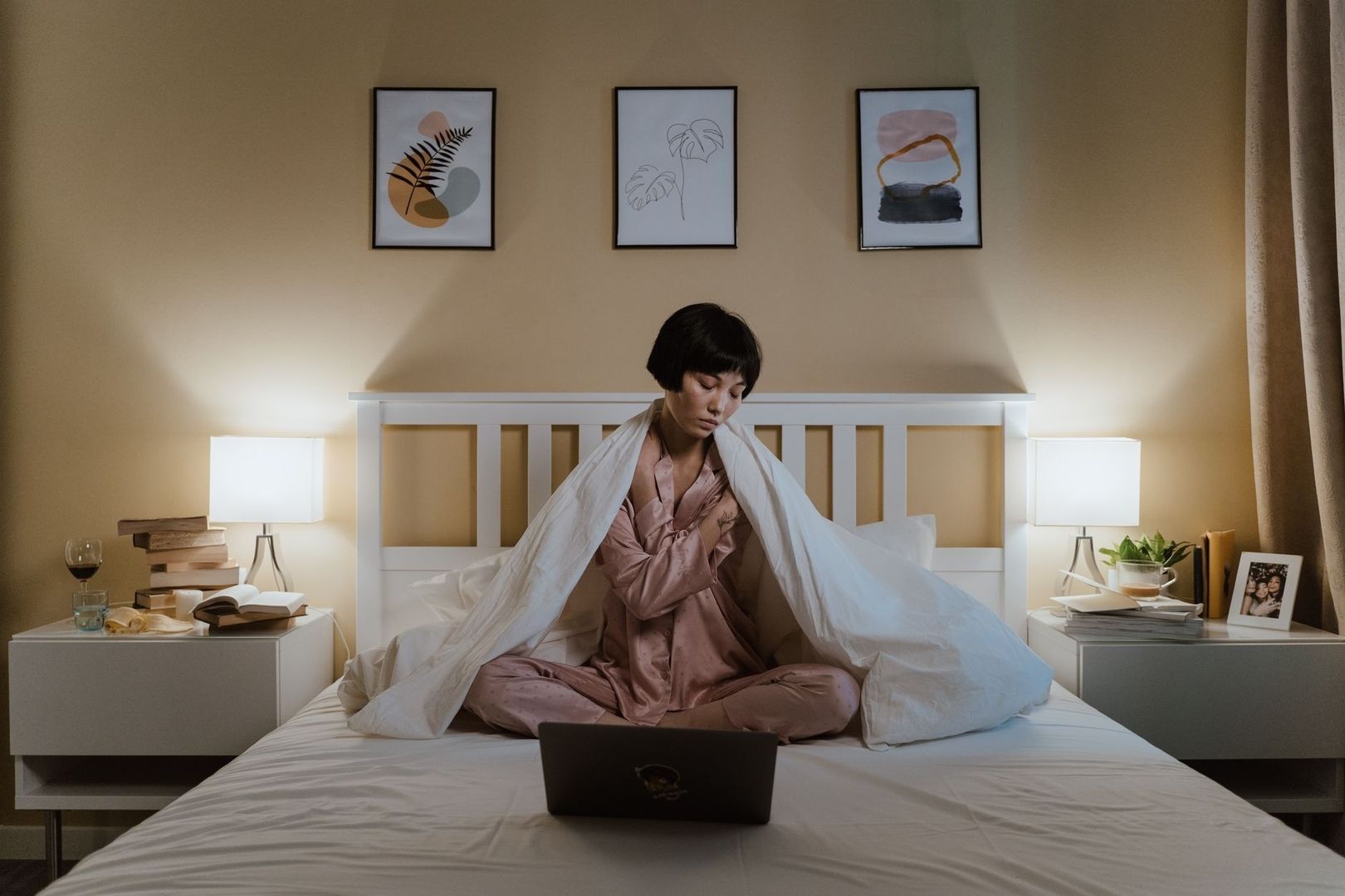 Persoon in pyjama zit met laptop op bed tijdens een rustige avond