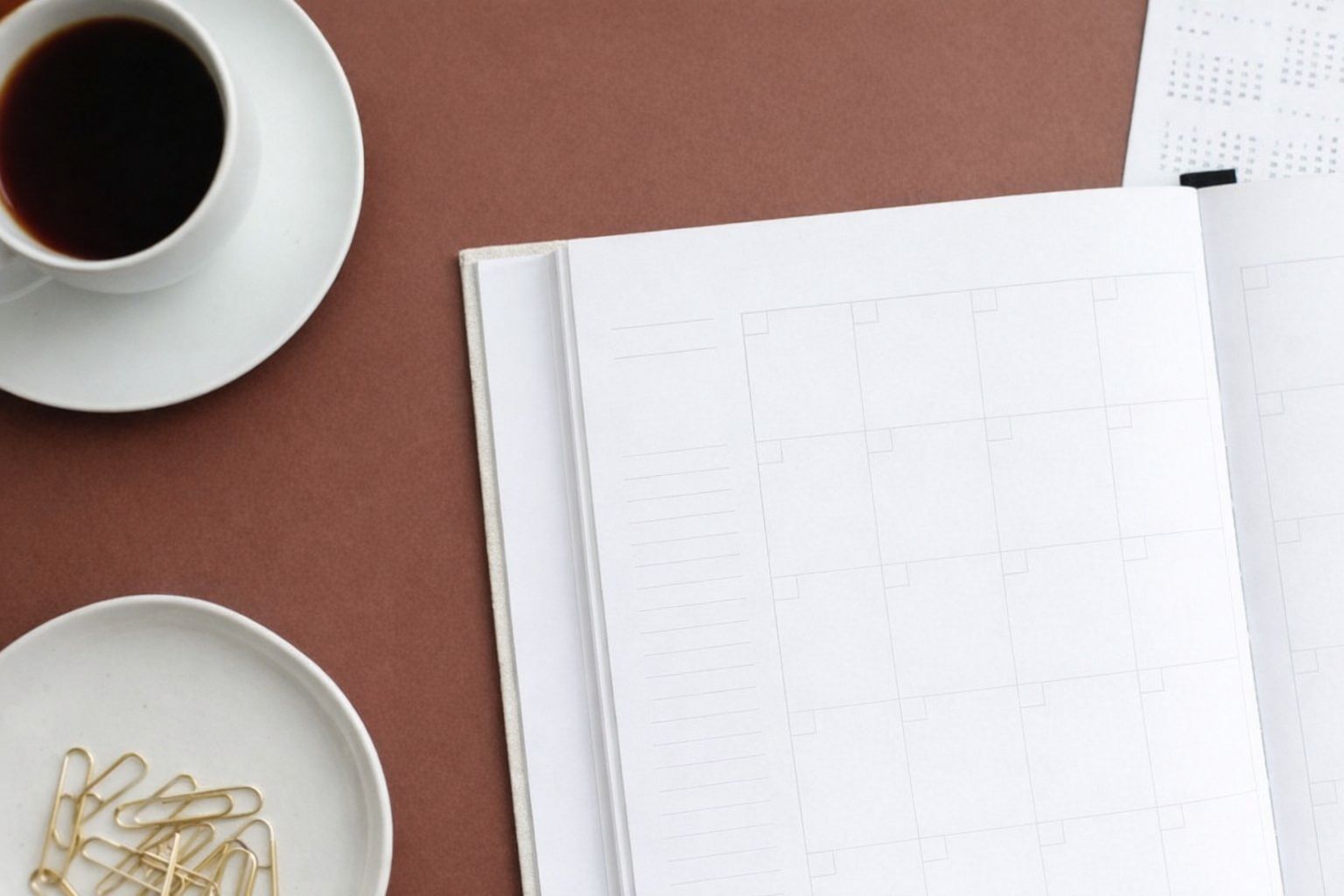Bovenaanzicht van een open planner, koffie en paperclips op een bureau.